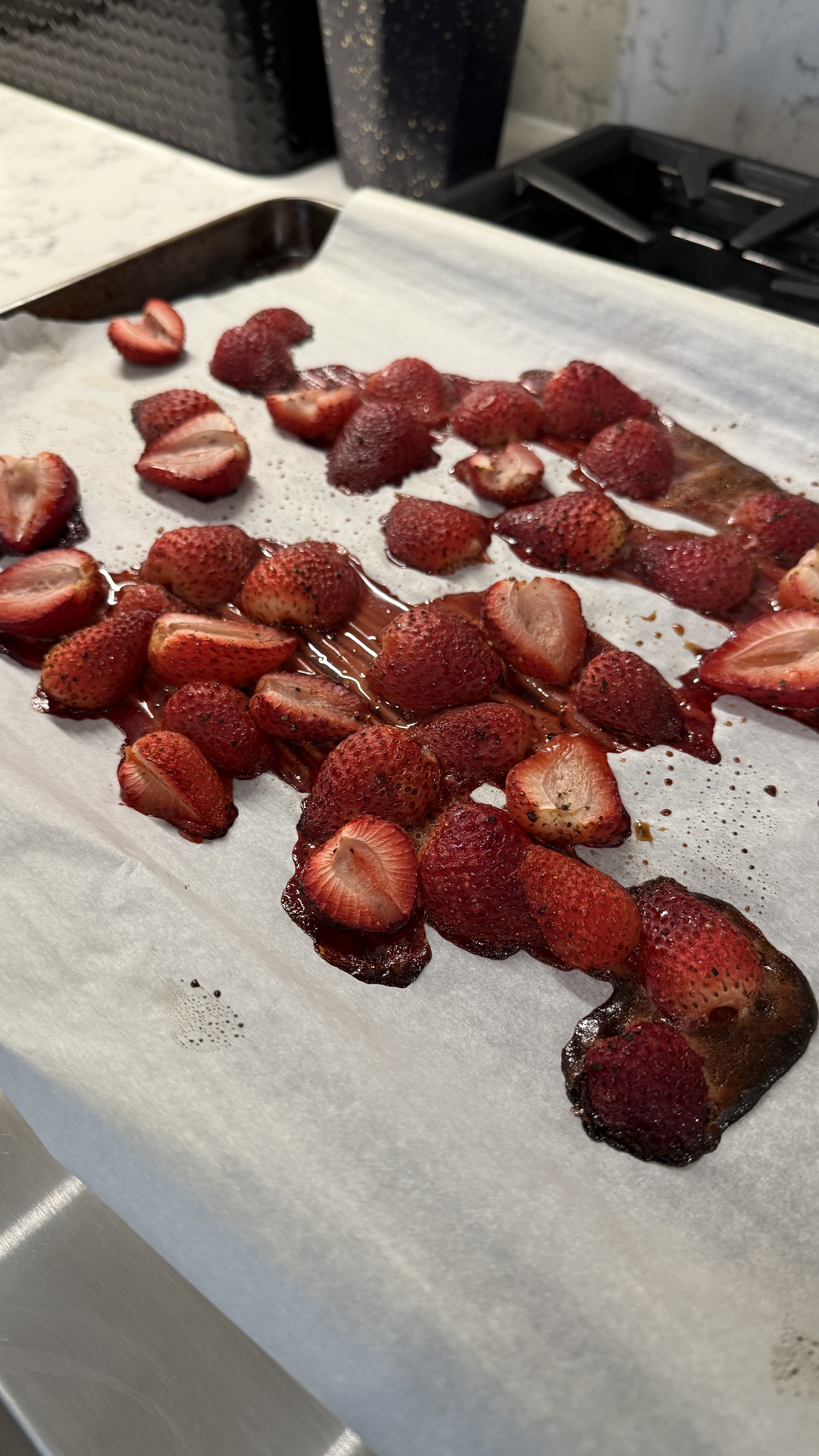 Roasted strawberries on a parchment-lined sheet pan, dark and juicy
